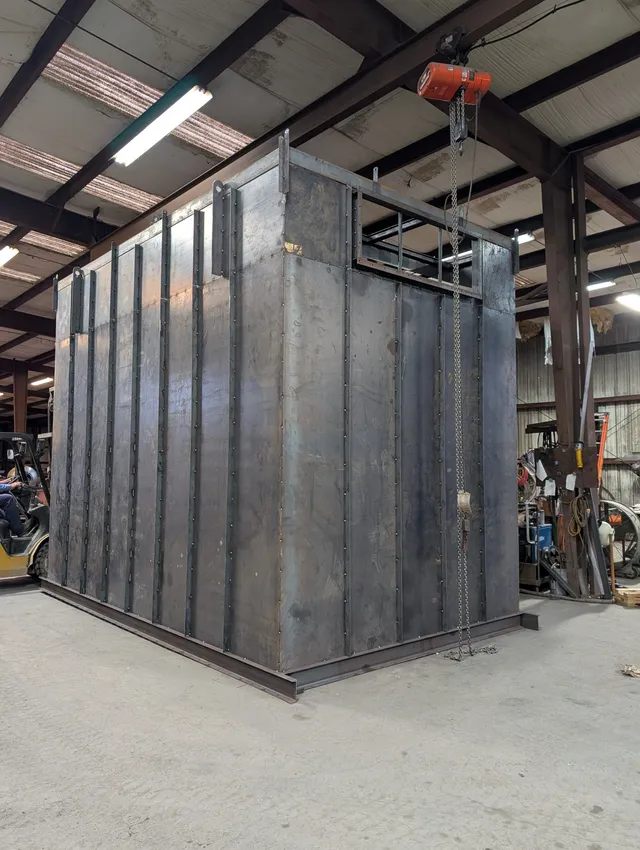 Large bare-steel enclosure being fabricated in the shop with overhead chain hoist